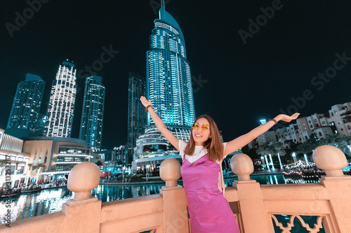 Photography Happy asian woman in dress raising hands in front of the skyscrapers in night city of Dubai, UAE