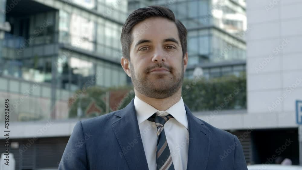 Handsome young businessman looking at camera. Portrait of cheerful bearded young businessman standing on street and smiling at camera. Business concept Handsome young businessman looking at camera. Portrait of cheerful bearded young businessman standing on street and smiling at camera. Business concept