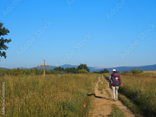 Pilgrim walking through beautiful landscape with cross on the road to Santiago de Compostela, Camino de Santiago, Way of St. James, Journey from Astorga to Foncebadon, French way, Spain