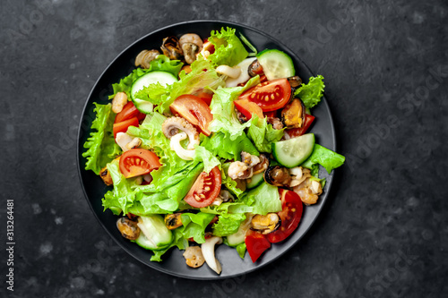 seafood salad, tomato, cucumber, sweet pepper, lettuce on a black plate on a stone background