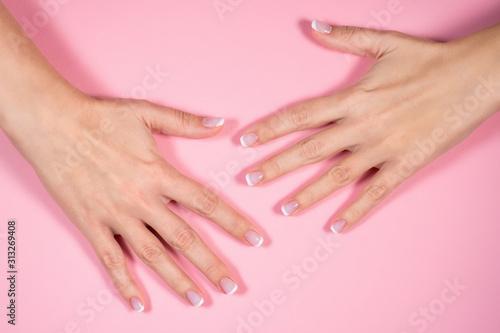 Closeup top view of two beautiful female hands with fresh professional french pink and white manicure isolated on pastel pink background. Horizontal color flatlay photography.