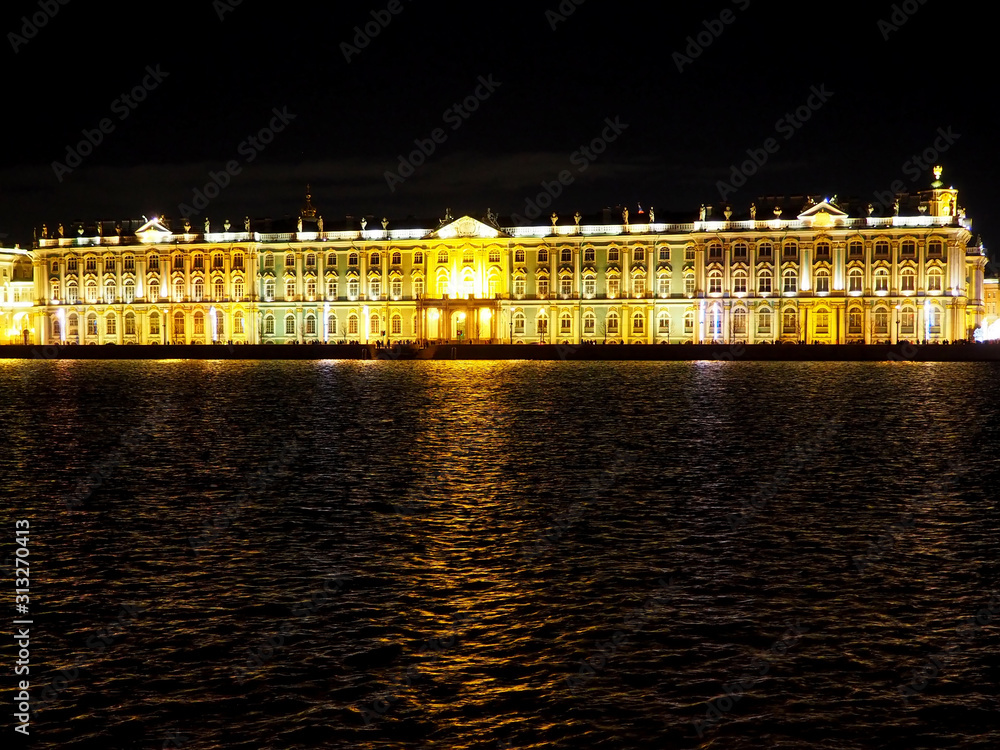 building facade illuminated by yellow lights reflecting in the water of a wide river at night