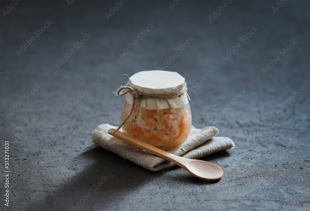 Sauerkraut with carrots and cumin in a jar on a linen napkin with a wooden spoon in a rustic style on a dark background Sauerkraut with carrots and cumin in a jar on a linen napkin with a wooden spoon in a rustic style on a dark background