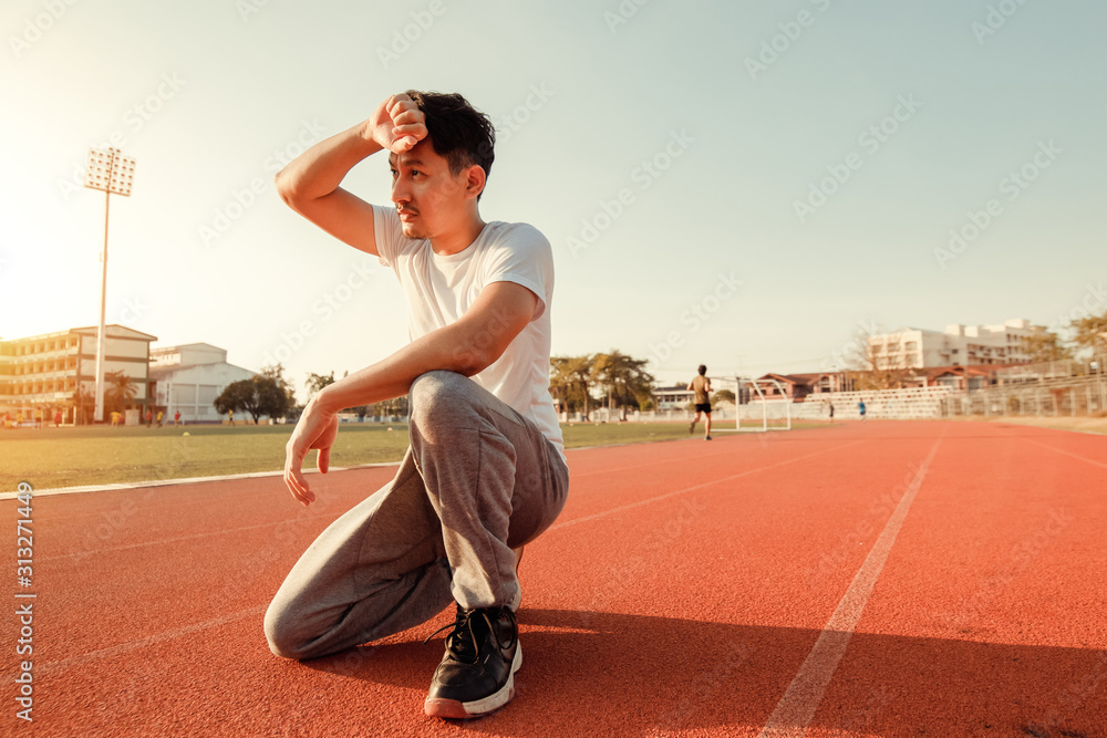 Fototapeta premium Tired wet athletic man wiping sweat his hand at sport stadium with sunset.