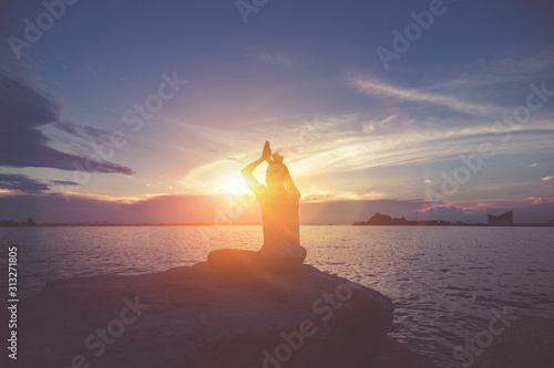 A women yoga on the rock near the sea with sunset sky.