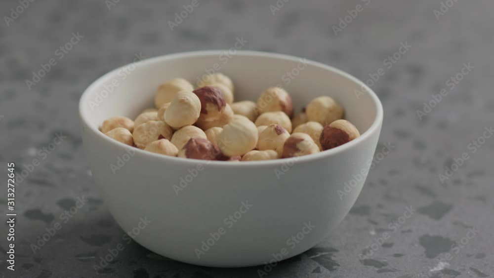 Slow motion roasted hazelnuts falling into white bowl on terrazzo countertop Slow motion roasted hazelnuts falling into white bowl on terrazzo countertop