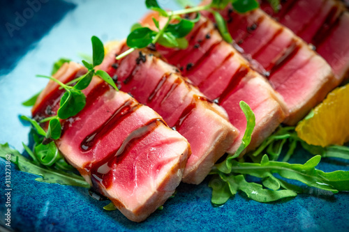 Sliced grilled tuna with green salad and tomatoes in a plate on a wooden background. Close up