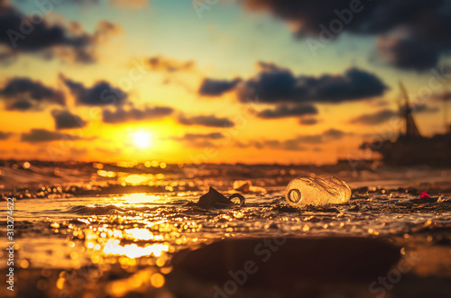 Plastic water bottle on the beach, environment pollution. Dirty beach and sunset.