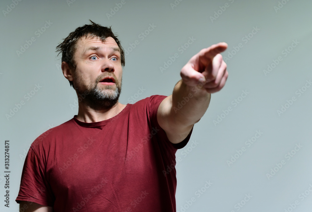 Portrait of a wild unkempt unshaven middle-aged man of 40 years in a burgundy t-shirt on a gray background. He stands right in front of the camera, talking, showing emotions. Waves his hands. Portrait of a wild unkempt unshaven middle-aged man of 40 years in a burgundy t-shirt on a gray background. He stands right in front of the camera, talking, showing emotions. Waves his hands.