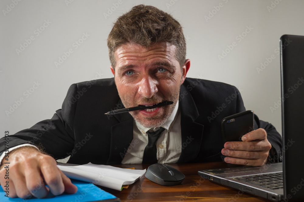 corporate business work stress - young desperate and frustrated businessman working stressed and overwhelmed at office computer desk biting pen feeling exhausted