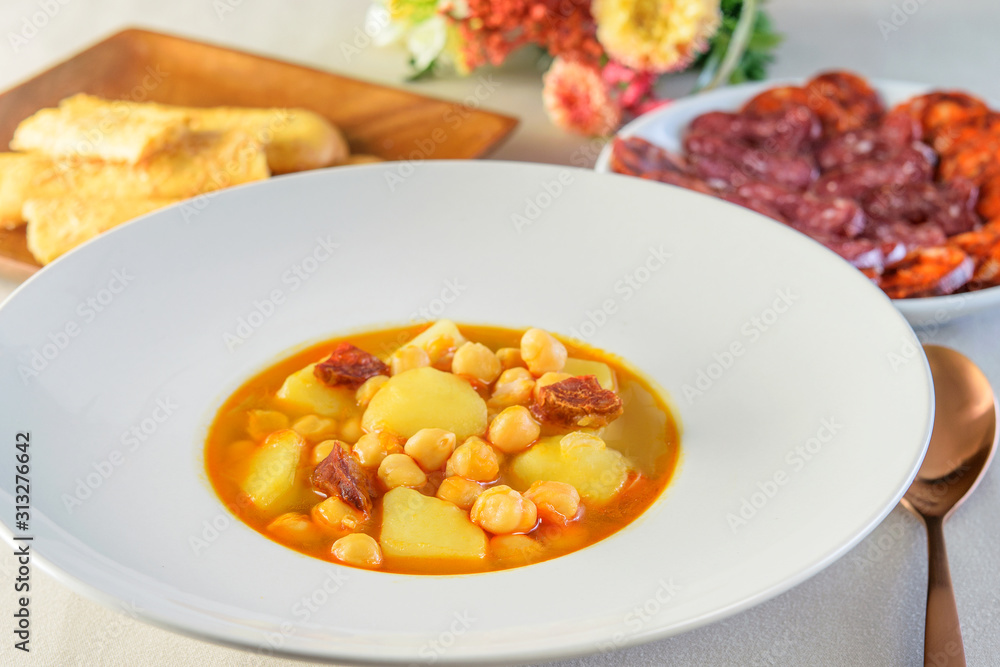 Hot soup sauce with sausages, potatoes and soybeans in the white dish, on the table served also with cheese sticks and sausage salami. Hot soup sauce with sausages, potatoes and soybeans in the white dish, on the table served also with cheese sticks and sausage salami.