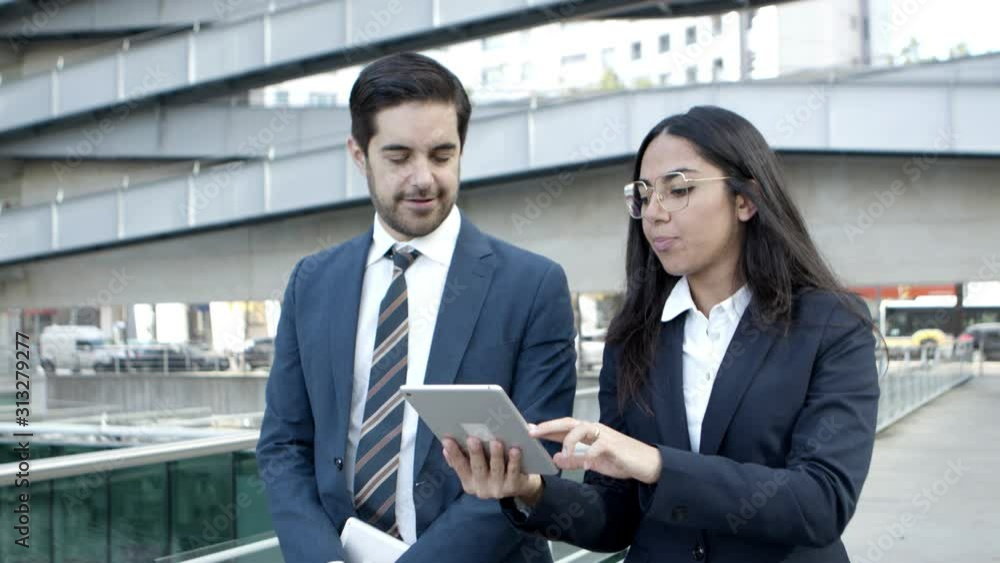 Businessman and businesswoman using tablet pc. Smiling young business colleagues walking and using digital tablet together on street. Wireless technology concept Businessman and businesswoman using tablet pc. Smiling young business colleagues walking and using digital tablet together on street. Wireless technology concept