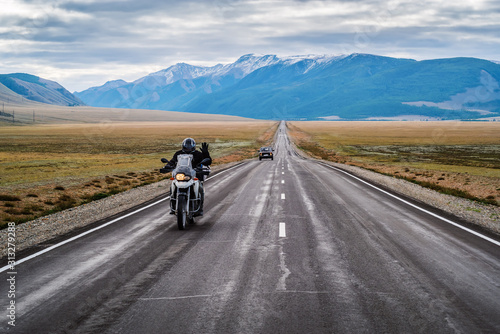 A motorcyclist with his hand raised in greeting, riding along the Chuysky highway at dawn, landscape with a highway. Russia, mountain Altai © vadim_orlov