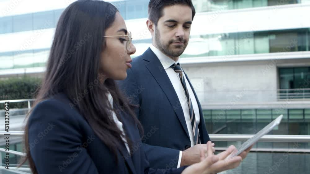 Business colleagues using tablet pc on street. Side view of smiling young businessman and businesswoman walking and using digital tablet together on street. Wireless technology concept Business colleagues using tablet pc on street. Side view of smiling young businessman and businesswoman walking and using digital tablet together on street. Wireless technology concept