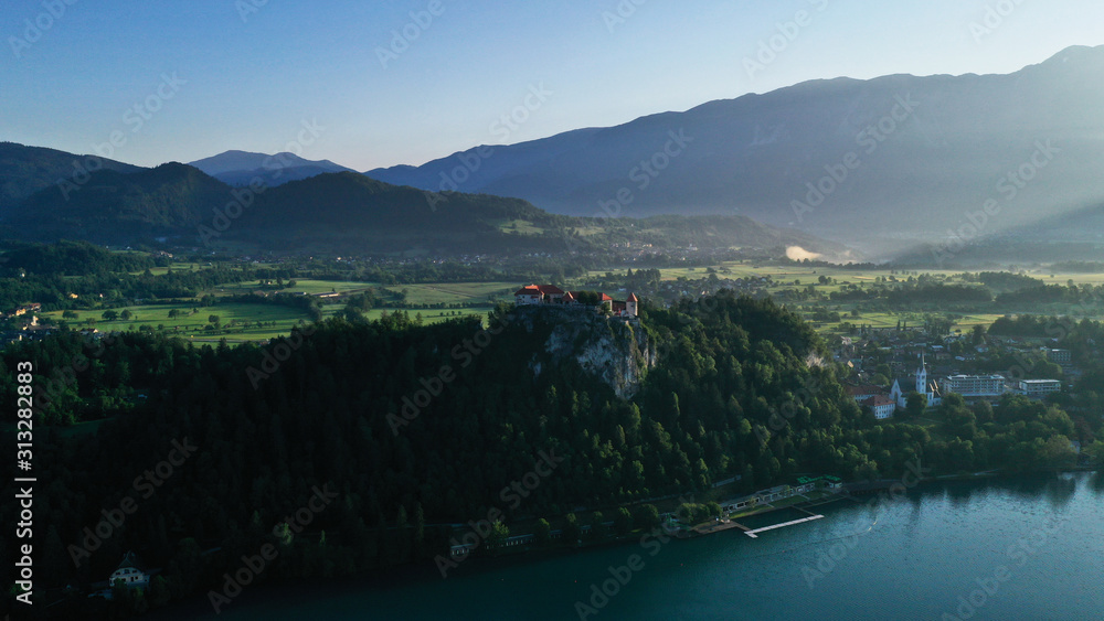 Aerial footage of Bled castle on rocky cliff, Lake Bled in Slovenia, Europe. Natural mountainous landscape around castle, green meadows and fields. Summer.