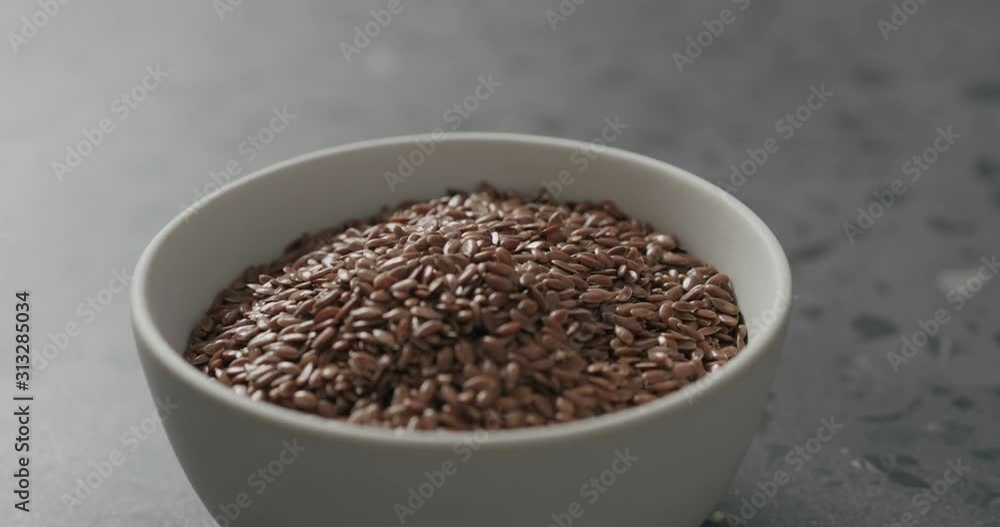 Slow motion handheld shot of flaxseed in white bowl on terrazzo countertop Slow motion handheld shot of flaxseed in white bowl on terrazzo countertop