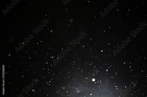 Snow and bokeh in the light of a lantern on a black background