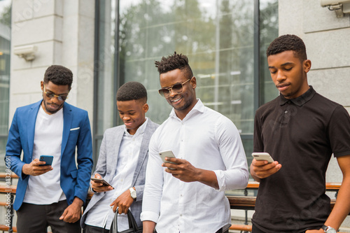 four young african men near the building in summer with phones in their hands