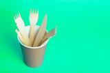 Wooden forks, knives and spoons for food in a paper cup on a colored background. Eco-friendly disposable tableware without plastic