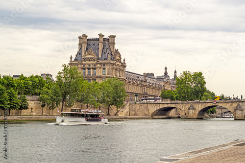 Photography looking across the river seine at the corner of the lourve palace art museum in paris france with a tourist boat crusing up the river