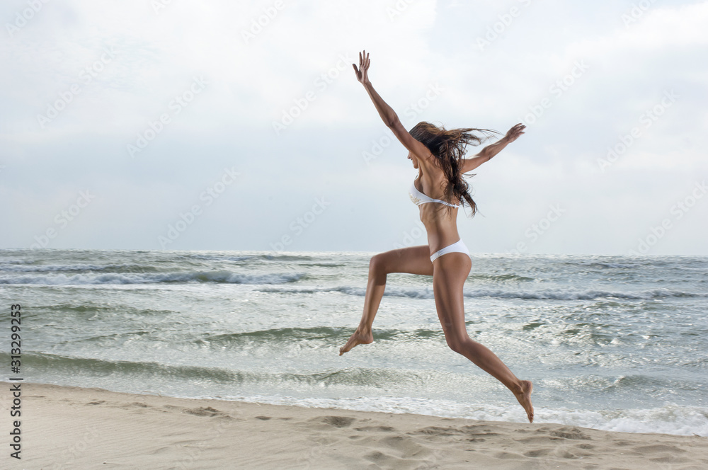 Ragazza in bikini bianco salta sulla riva del mare Ragazza in bikini bianco salta sulla riva del mare