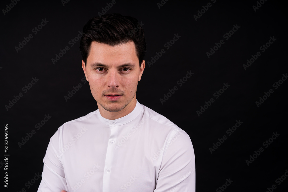 serious guy looking at the camera. Dressed in a white shirt, black background serious guy looking at the camera. Dressed in a white shirt, black background
