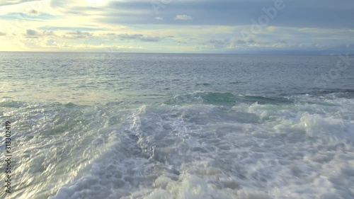 A panoramic view of ocean with seaweed and rock on beach with big high tide waves and splashes in the evening