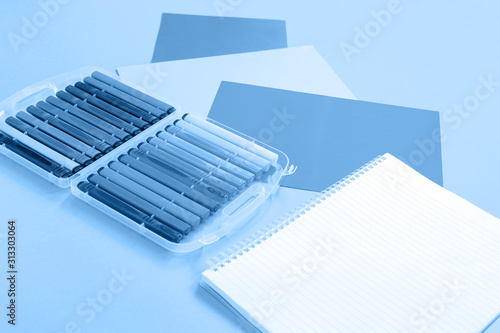 Fototapeta Naklejka Na Ścianę i Meble -  Trendy monochromatic white and blue color stationery, set of markers and notepad flat lay with copy space background. Minimal design for creative school or office concept