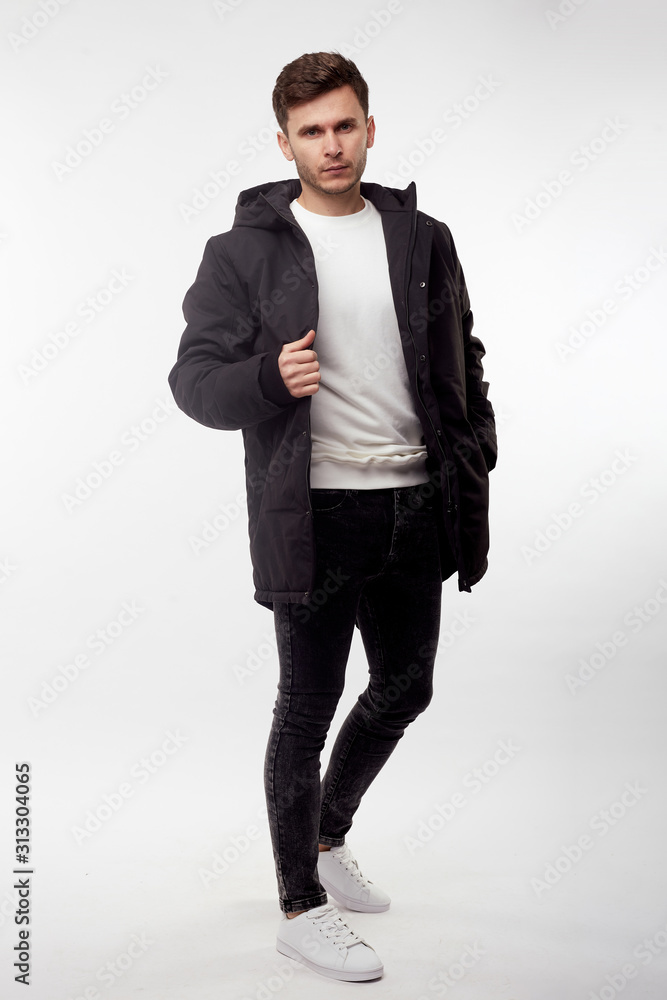 Young european man in white sweater and black pants, black down jacket posing on white background. Isolated. Young european man in white sweater and black pants, black down jacket posing on white background. Isolated.