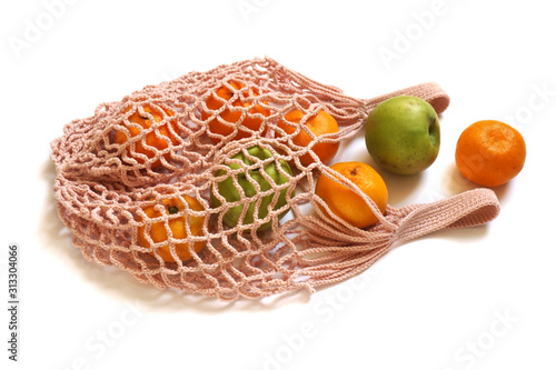 Peach Coloured Hand-Made Crochet Eco-Friendly String Shopping Bag with Green Apples and Tangerines  on White Background. Concept of Ecology, Environmental Protection & Zero Waste