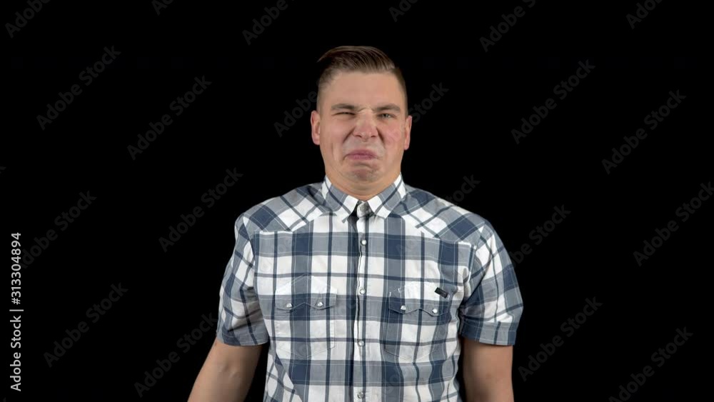 A young man takes off his mask and shows an emotion of disgust on his face. The man is unpleasant. A man hides his face behind a white mask on a black background A young man takes off his mask and shows an emotion of disgust on his face. The man is unpleasant. A man hides his face behind a white mask on a black background