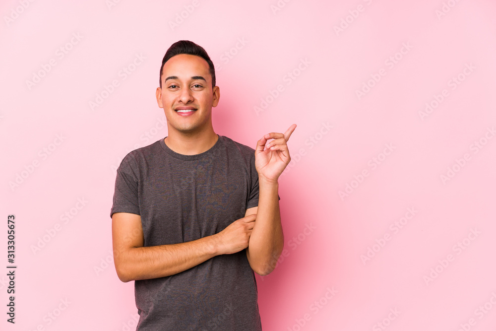 Yooung latin man posing in a pink backgroundsmiling cheerfully pointing with forefinger away. Yooung latin man posing in a pink backgroundsmiling cheerfully pointing with forefinger away.