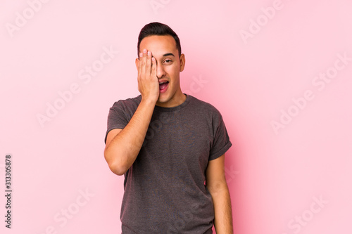 Yooung latin man posing in a pink backgroundhaving fun covering half of face with palm. photo