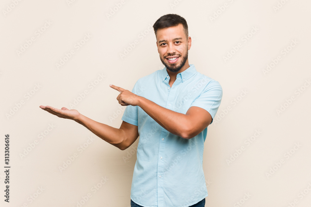 Young south-asian man excited holding a copy space on palm.