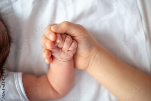 Closeup of a sister hand who hold the hand of one month little sister. Top view