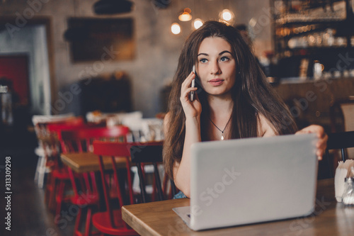 Business woman talking to the phone, working on a laptop and drinking coffee in a cafe. © zadorozhna