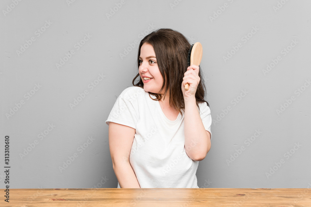 Young caucasian curvy woman holding a hair brush isolated on a grey background Young caucasian curvy woman holding a hair brush isolated on a grey background