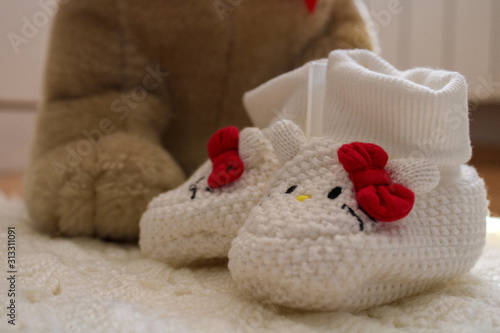 Knitted baby shoes for girl with big teddy bear in background