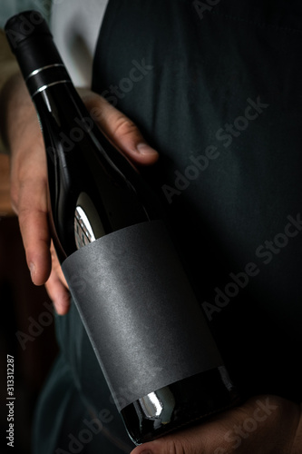 A full Bottle of wine in the hands of a male sommelier with a black label. Mock-up for red wine design. © Andrey
