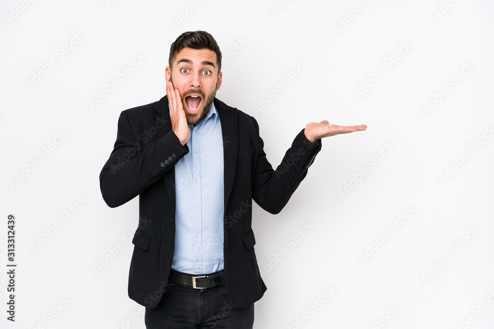 Young caucasian business man against a white background isolated holds copy space on a palm, keep hand over cheek. Amazed and delighted. Young caucasian business man against a white background isolated holds copy space on a palm, keep hand over cheek. Amazed and delighted.
