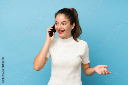 Young brunette girl over isolated blue background keeping a conversation with the mobile phone with someone