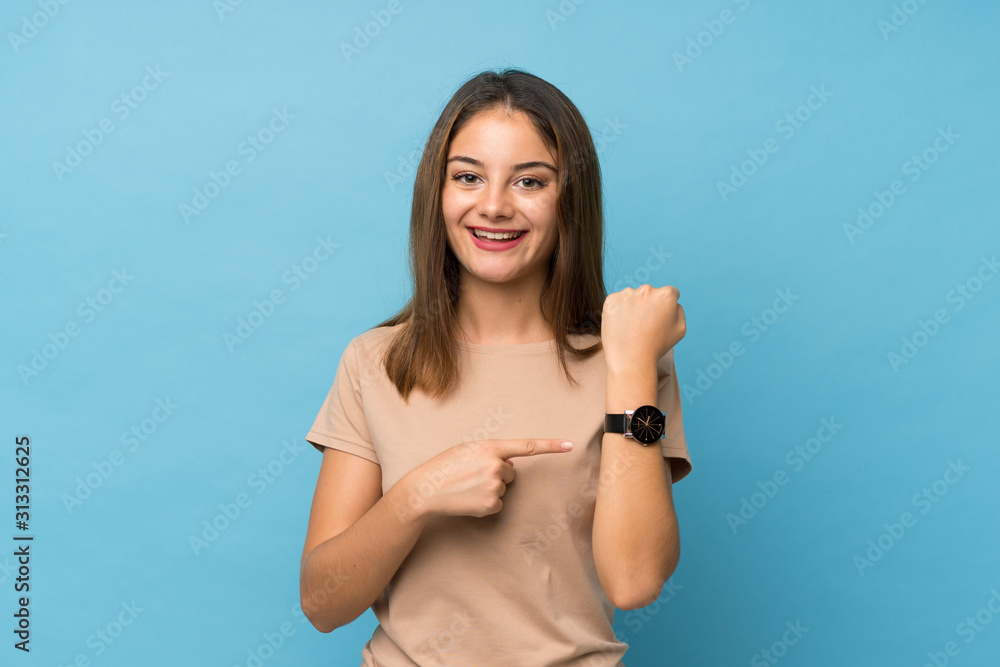 Young brunette girl over isolated blue background showing the hand watch - obrazy, fototapety, plakaty 