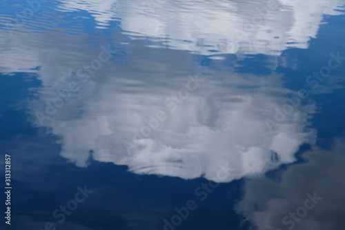 Reflection of fluffy clouds on the water surface. Blue and white colors dominates.