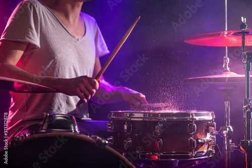 The drummer plays the drums. Beautiful blue and red background, with rays of light. Beautiful special effects smoke and lighting. The process of playing a musical instrument. Close-up photo.