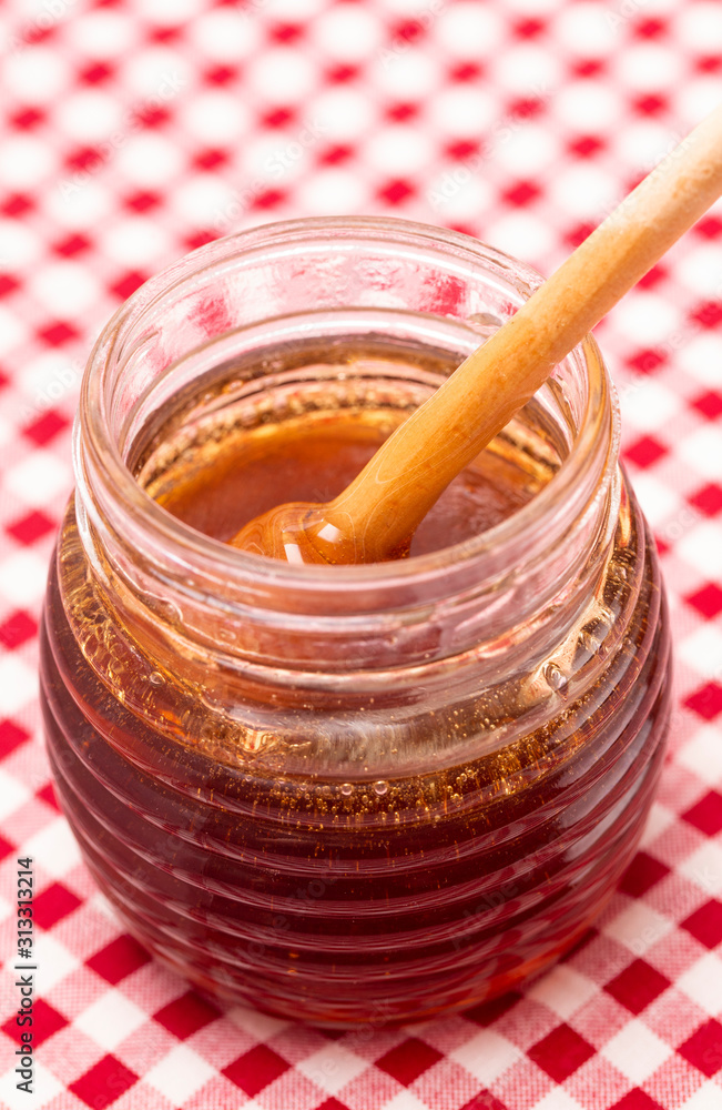 Fototapeta premium Jar of Fresh Raw Organic Honey on a Red and White Table Cloth