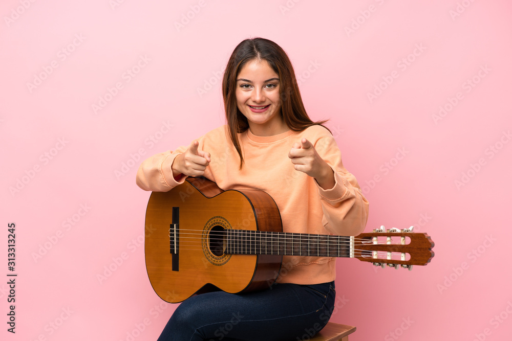 Young brunette girl with guitar over isolated pink background points finger at you with a confident expression Young brunette girl with guitar over isolated pink background points finger at you with a confident expression
