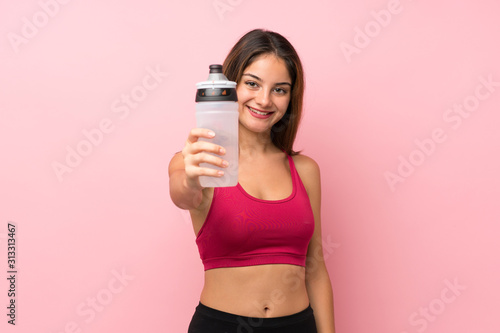 Young sport girl over isolated pink background with sports water bottle
