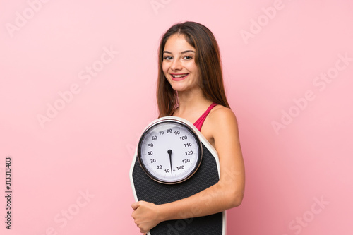 Young sport girl over isolated pink background with weighing machine