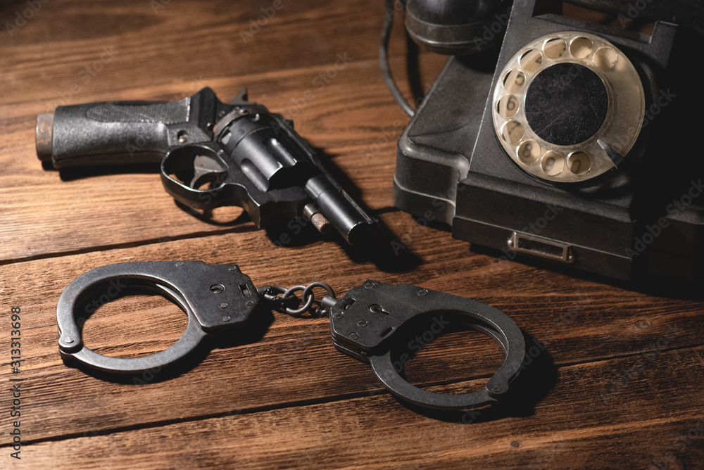 Obraz premium Black pneumatic gun, bracelets and old telephone on the table. Detective agent desk concept.