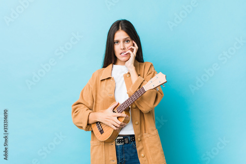 Canvastavla Young caucasian woman holding a ukelele biting fingernails, nervous and very anxious